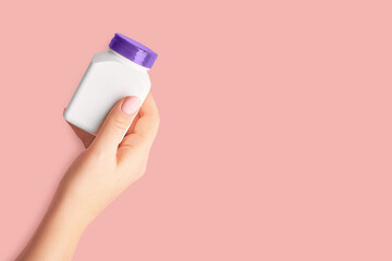 Female hand holding a jar of pills on a pink background