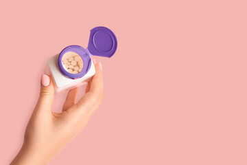 Female hand holding an open jar of pills on a pink background