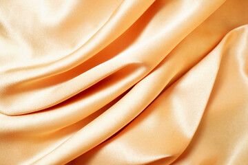 Close-up of yellow silk satin, draped fabric, gold color, elegant background. Beautiful wavy area...