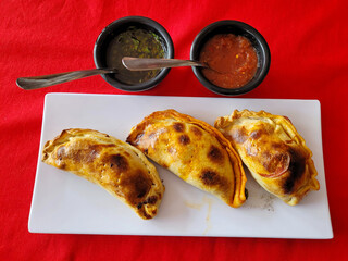 Three delicious Argentine empanadas with a crispy crust, served hot with sauces, restaurant