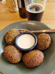 Vertical view of A plate of golden-brown falafel served with tahini sauce, paired with a dark stout