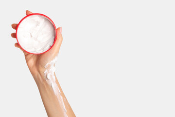 A woman's hand holds a jar of cream and applies it to her hand. On a light background.