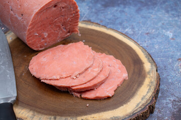 Vegan ham made of wheat gluten, shaped and cooked in a ham press. Sliced, wooden board.