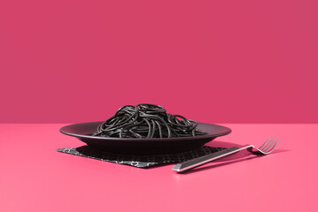 Espaguetis con tinta de calamar negro en un bol con tenedor sobre fondo rosa	