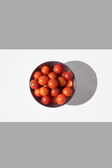 Tomates cherry maduros en un bol  sobre fondo gris y blanco. Vista superior	
