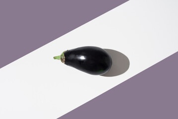Una berenjena fresca sobre un soporte blanco y fondo morado. Vista superior	