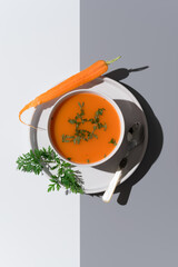 Sopa de zanahoria adornada con perejil fresco en un plato sobre fondo gris y blanco. Vista superior