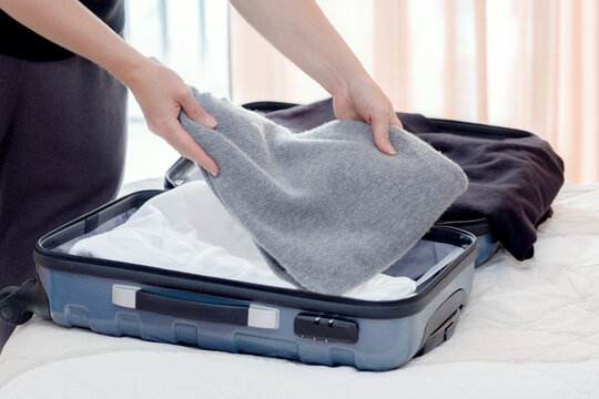 Woman is going on a trip and puts in a blue suitcase a gray wool sweater and other warm things. Close-up