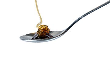Honey flows onto a teaspoon. Isolated on white