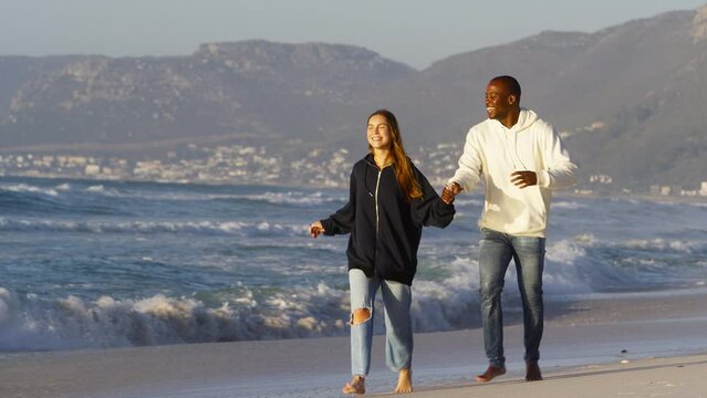 Full length shot of casually dressed loving young couple running hand in hand along sandy shoreline against beautiful sunrise morning over beach and sea in South Africa - shot in slow motion