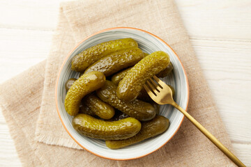 Marinated gherkins in a bowl on a light wooden background. Homemade pickles. Close-up