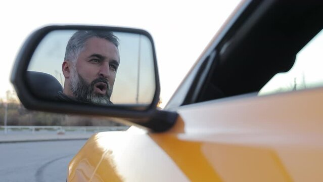 Singing Man's Reflection in Car Mirror, Close-up reflection of a man passionately singing in the side mirror of a yellow convertible car.
