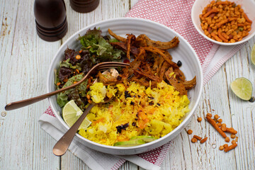 Vegan rice pilaf, seitan and salad bowl served in a white ceramic bowl, wooden table, stylish traditional setup