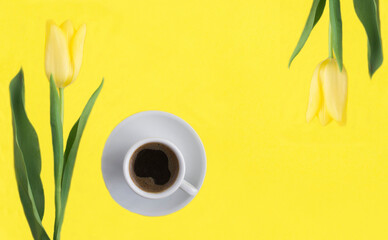 Black coffee in the white cup and yellow tulip on the yellow  background. Top view. Copy space.