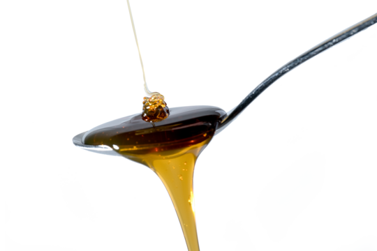 Honey drips onto the spoon, runs off the edge of the spoon again, isolated on transparent background