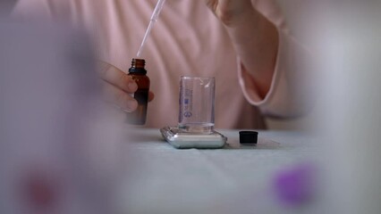 Detail cropped shot of unrecognizable female artisan craftperson dropping essential oil into glass bottle using pipette. Process of making handmade natural scented candle at workshop, slow motion.