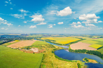 Sunny day in the village. Rural landscape in daylight. Aerial view of a meandering river, cultivated fields, and a beautiful cloudy sky.