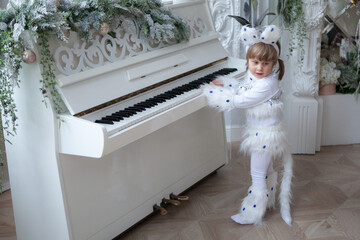 A little girl in a white cat costume is playing on white piano by the Christmas decorations