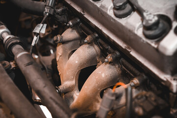 A close-up of a car rusted and old exhaust manifold under the hood.
