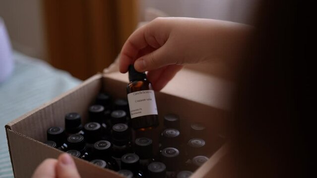 Closeup view from shoulder of female artisan craftperson choosing scented perfume for creating candle building mixture. Process of making handmade natural scented candle at workshop, slow motion.