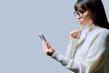 Profile view middle aged woman using smartphone on grey background