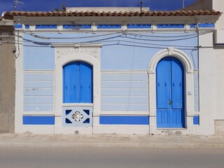 Una casetta bianca e azzurra, con porta blu e finestra blu.