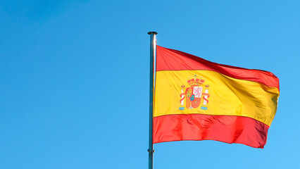 Spanish flag waves in the wind against a blue sky, banner blowing like soft silk