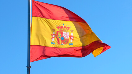 Spanish flag waves in the wind against a blue sky, banner blowing like soft silk