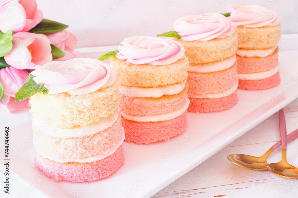 Poster spring mini cakes with buttercream rose. table scene with a white wood background. pink layers with 
