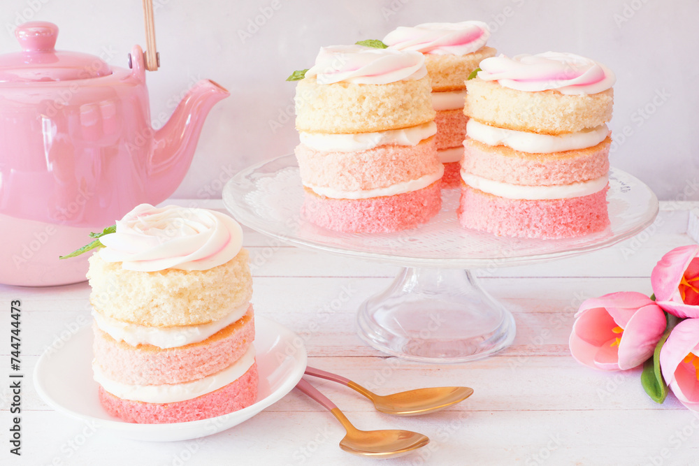 Poster spring mini cakes with buttercream rose. table scene with a white wood background. pink layers with 