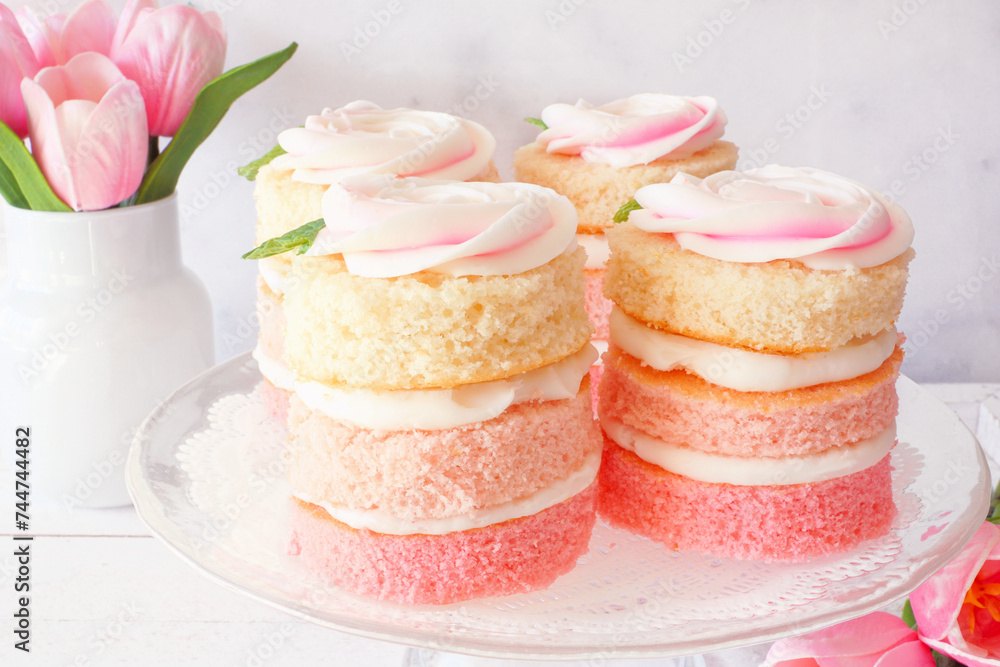 Poster spring mini cakes with butter cream rose. table scene with a white wood background. pink layers with
