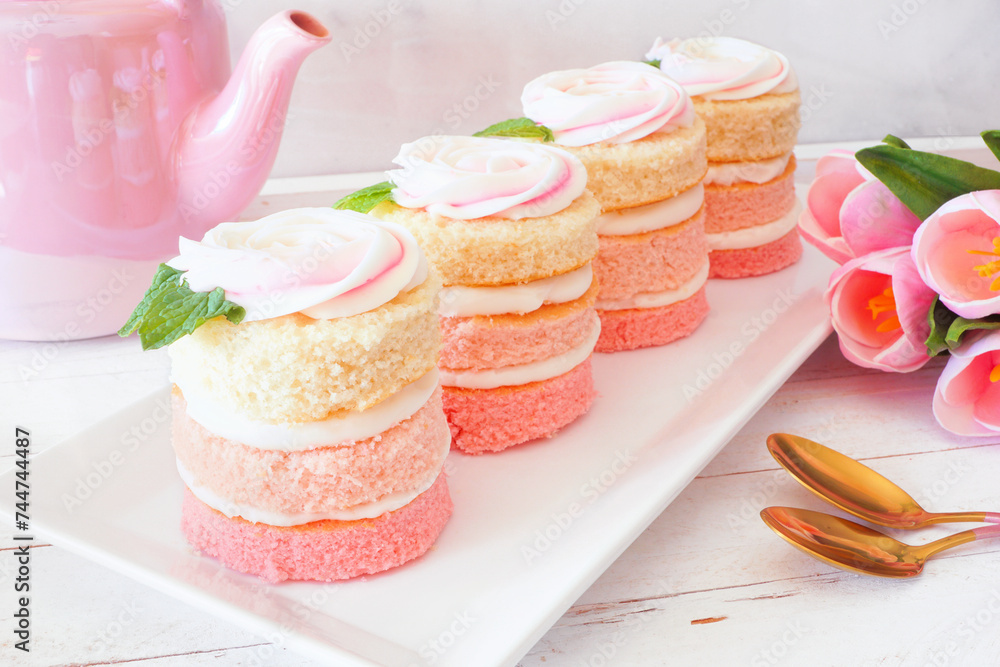 Poster spring mini cakes with buttercream rose. table scene with a white wood background. pink layers with 