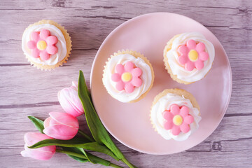 Plate of pink spring flower cupcakes. Overhead view table scene with a wood background.