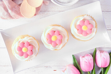 Obraz na płótnie Canvas Plate of pink spring flower cupcakes. Above view table scene with a white wood background.
