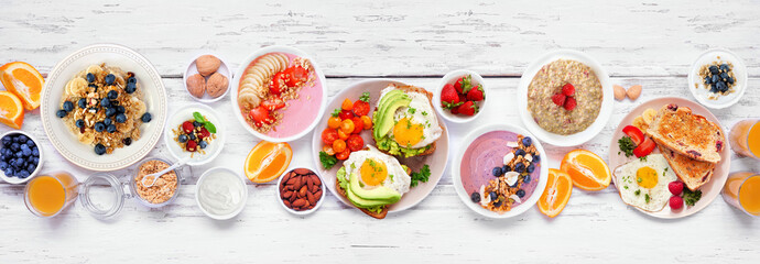 Healthy breakfast or brunch table scene on a white wood banner background. Overhead view. Avocado toast, smoothie bowls, oats, yogurt and a variety of nutritious foods. - obrazy, fototapety, plakaty
