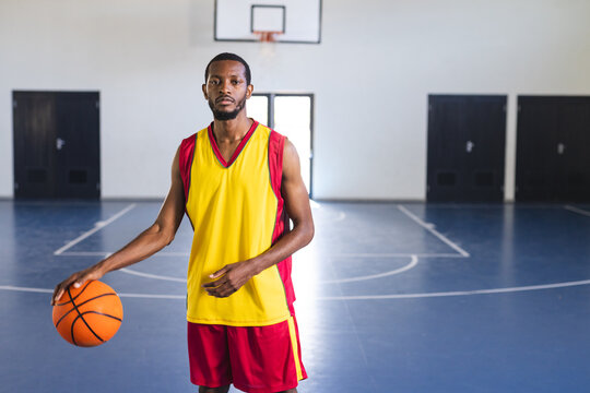 African American man holds a basketball in a gym, with copy space