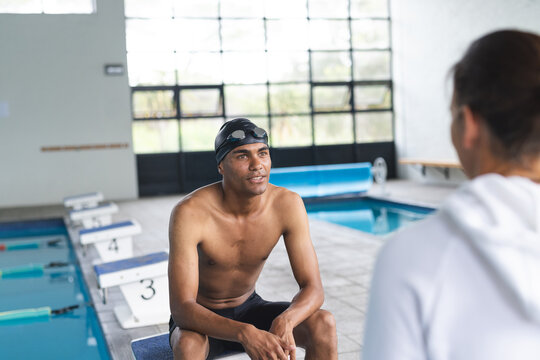 Young biracial male athlete swimmer sits by the poolside, engaging in conversation - Powered by Adobe