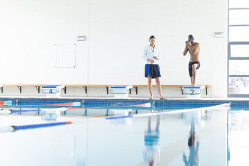 Coach timing swimmer's lap in an indoor pool, with copy space