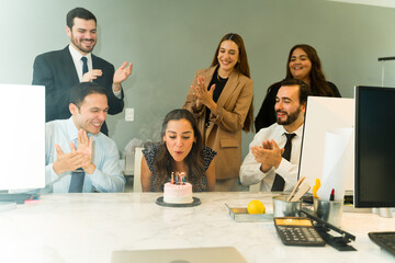 Cute Latin woman blowing the candles of a cake while celebrating. her birthday in an office