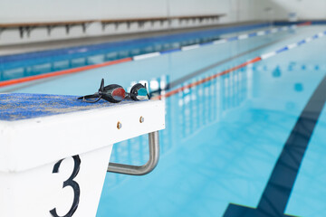Swimming goggles rest on the edge of a pool at the starting block with copy space