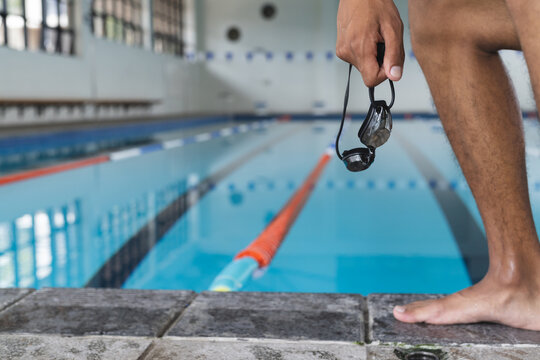 Close-up of a young biracial male athlete swimmer holding swimming goggles at the poolside with copy
