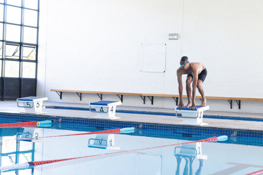 African American male athlete swimmer prepares to dive into a swimming pool at an indoor facility
