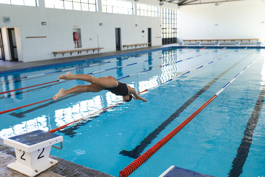 Caucasian female athlete swimmer dives into a swimming pool at an indoor facility