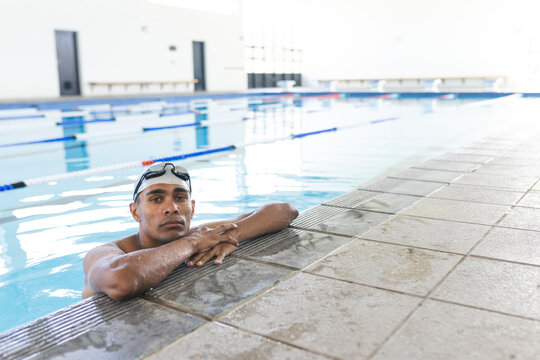 Young biracial male athlete swimmer rests at the poolside after swimming, with copy space - Powered by Adobe