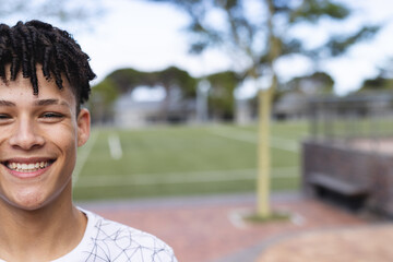 Teenage biracial boy smiles at an outdoor sports field, with copy space