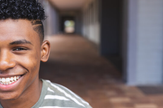 Teenage biracial boy smiles brightly in a high school corridor with copy space