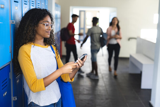 Young biracial woman checks her phone in a high school hallway with copy space