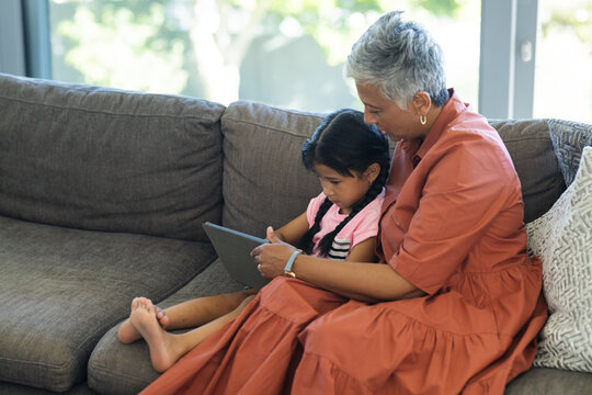 Grandmother and biracial granddaughter enjoy a tablet together on the sofa at home