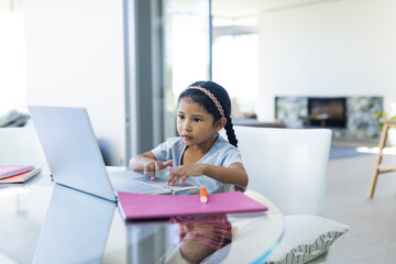 Biracial girl focuses on her laptop at home