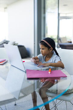 Biracial girl focuses on her laptop at home